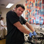 Han reparerar en maskin. Men kroppsspråket, uttrycket och sjukhusmiljön gör att han liknar en kirurg som opererar.