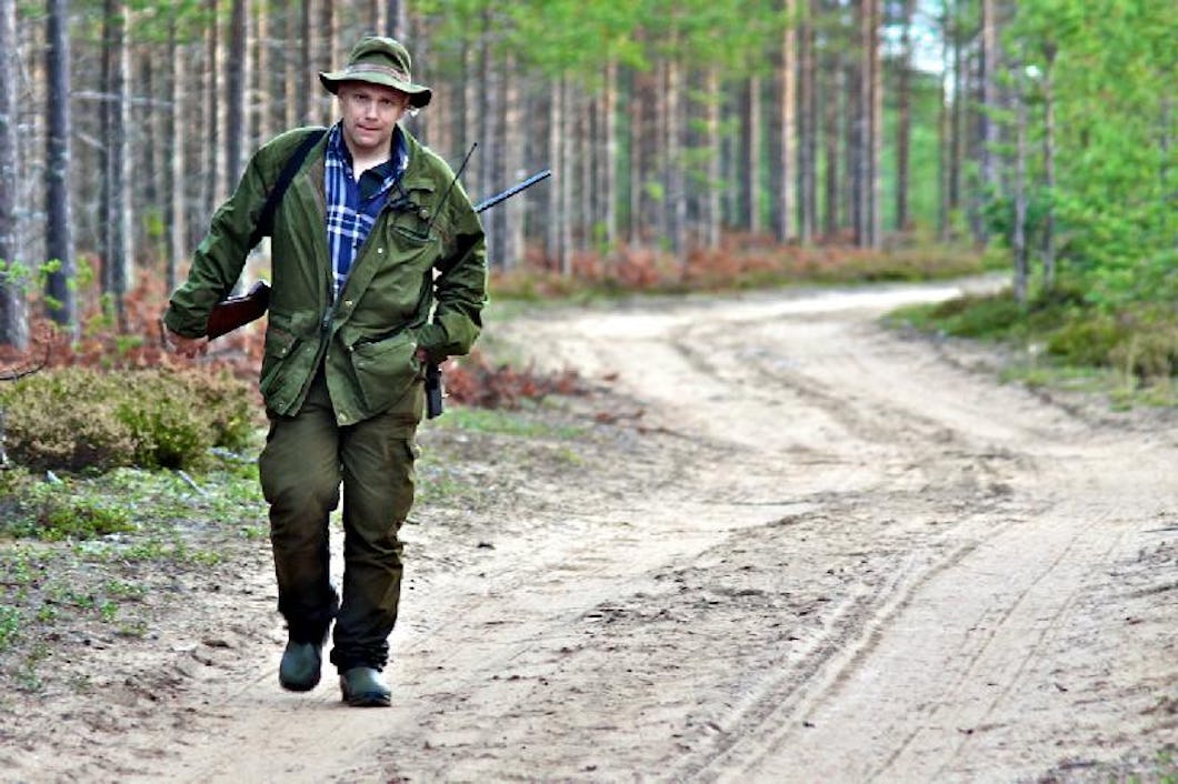 En man kommer och går längs en skogsväg, klädd för jakt.