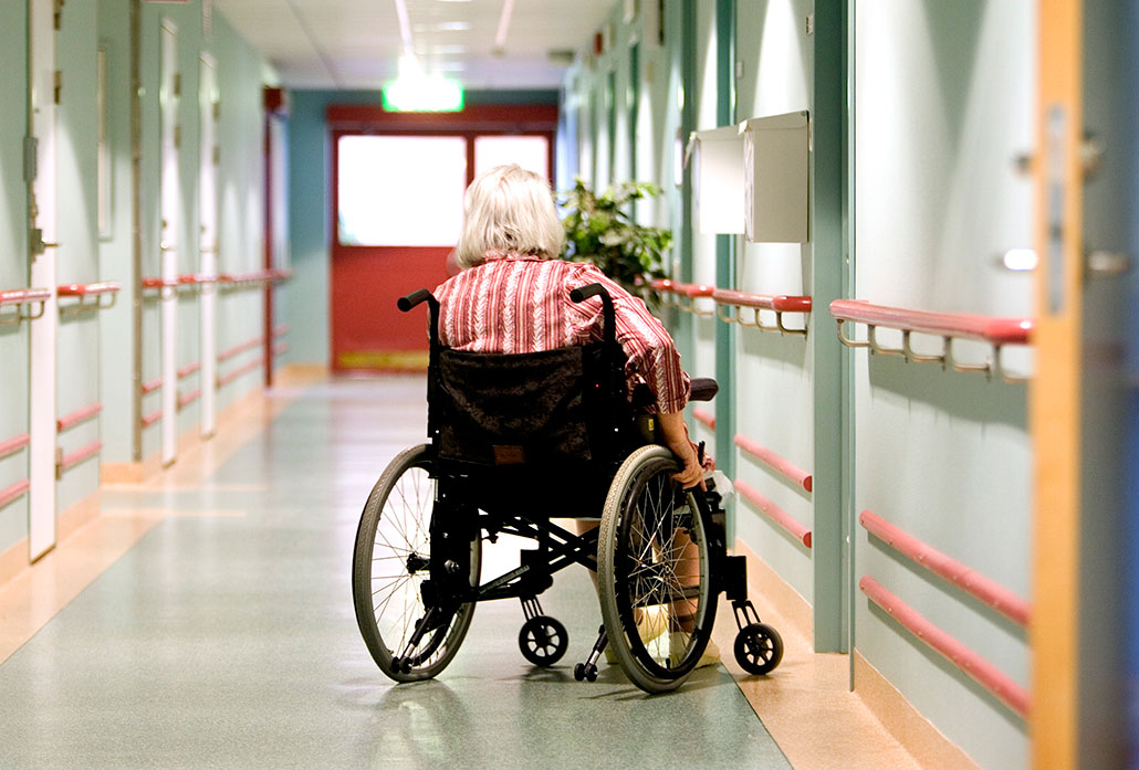 En äldre person sitter i en rullstol i en tom korridor.