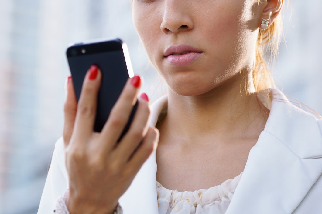 En person med målade naglar håller en mobiltelefon och tittar på skärmen med ett allvarligt ansikte. Personen har på sig en vit topp och en jacka.