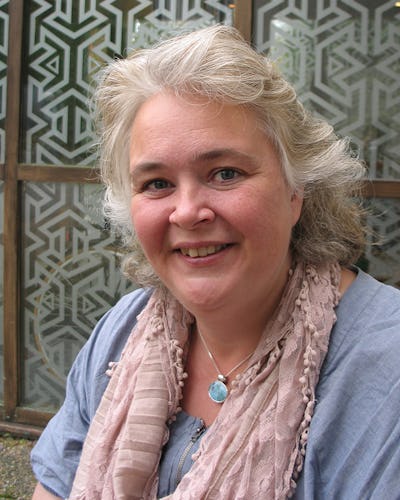 Camilla Claesson iklädd en ljusblå topp och en rosa halsduk, står framför ett mönstrat glas.