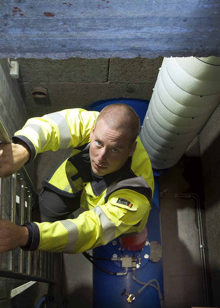 En person i gula reflexkläder klättrar ned för en stege.