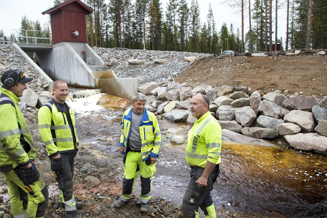 Fyra personer i gula reflexkläder står tillsammans framför en kraftverksdamm.