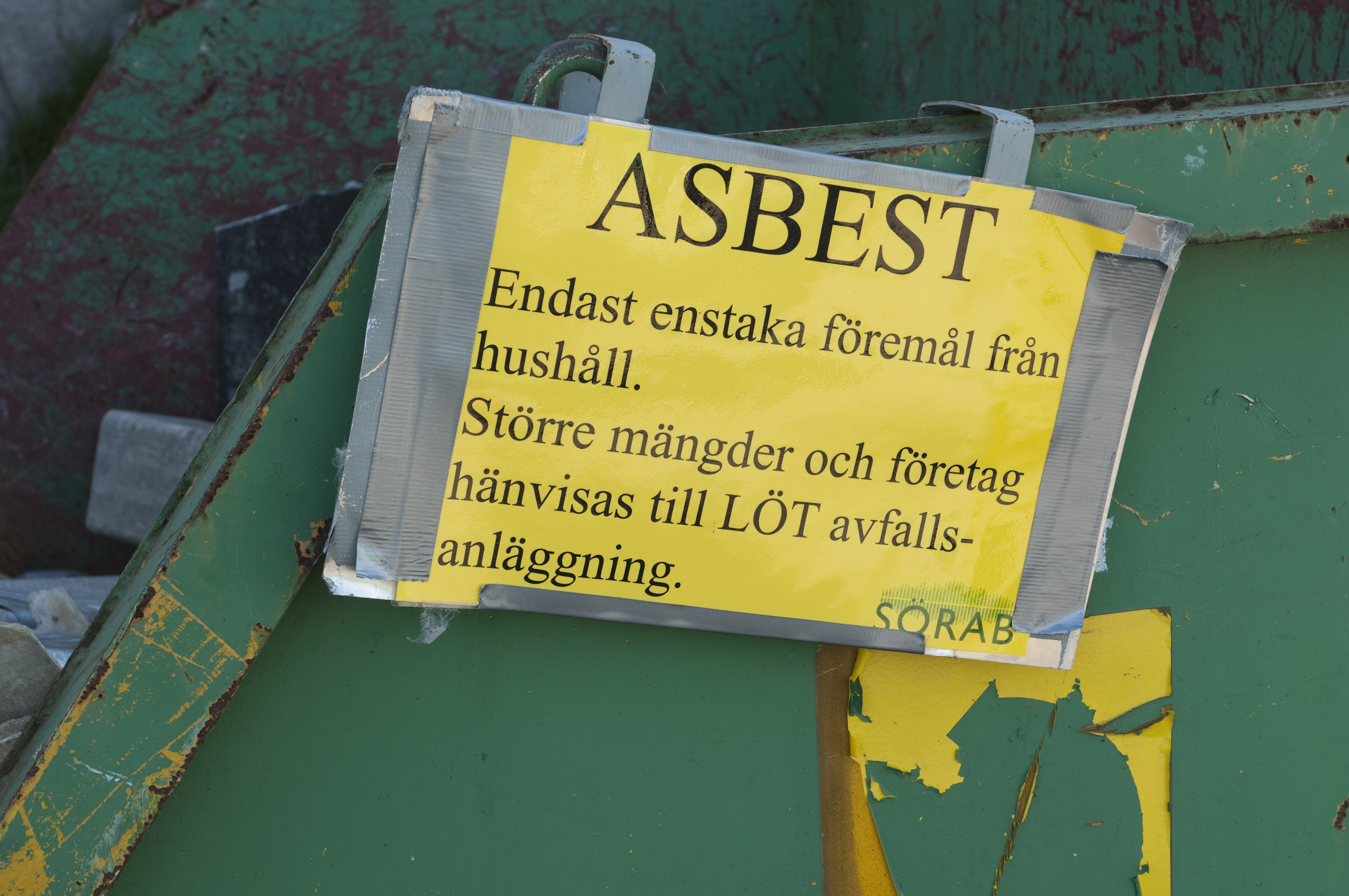 En grön container med en skylt där det står: "Asbest. Enstaka föremål från hushåll. Större mängder och företag hänvisas till LÖT avfalls-anläggning. Sörab."
