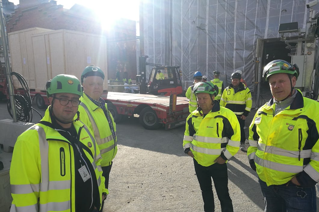 En grupp skyddsombud i gula reflexjackor står på en arbetsplats utomhus.
