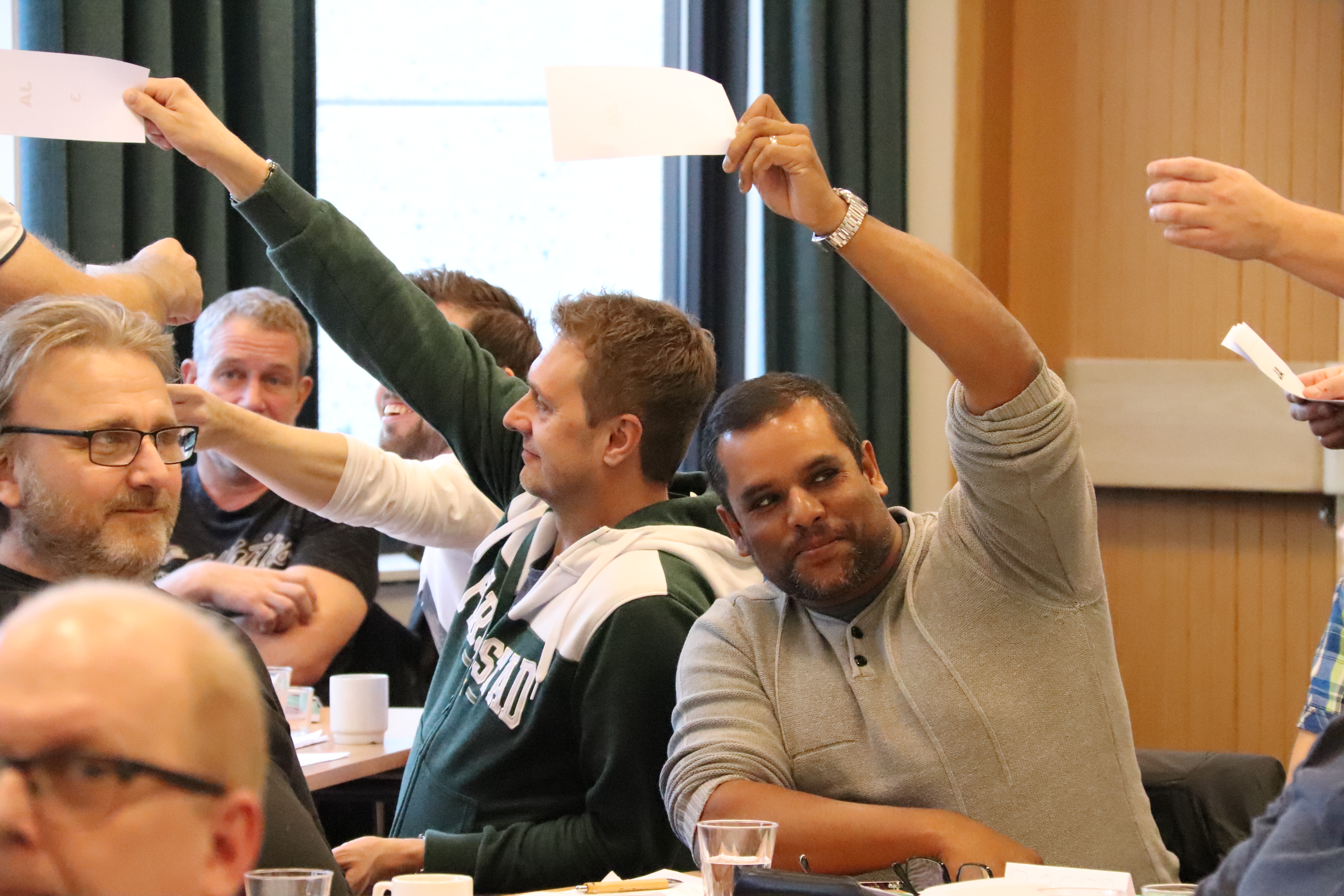 Mötesdeltagare som håller upp röstlappar i luften.