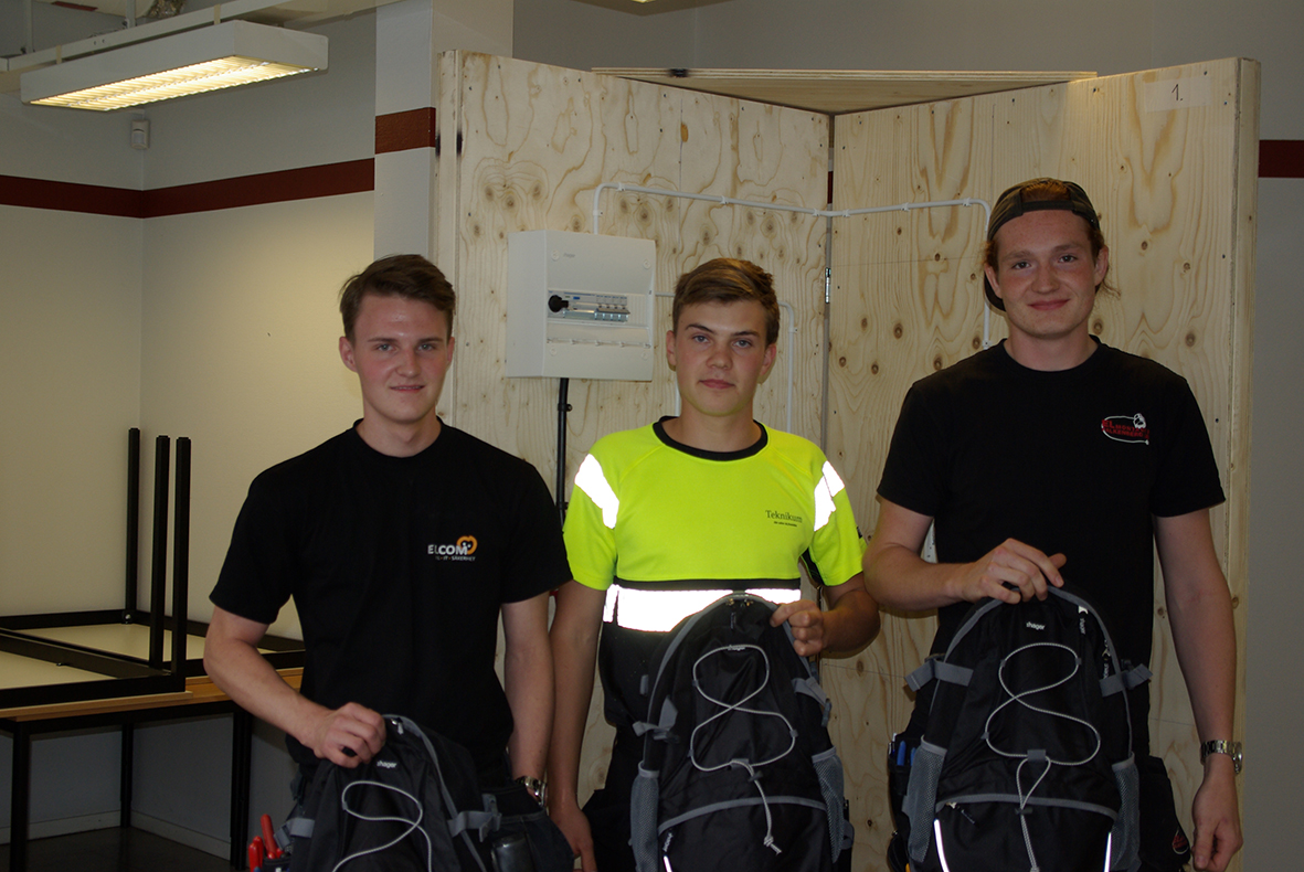 Tre personer står framför en plywood-vägg med varsin ryggsäck i händerna.