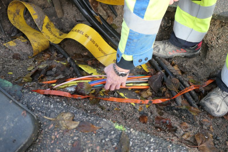 En hand sträcker sig ned i ett hål i marken med ett virrvarr av sladdar och kablar i