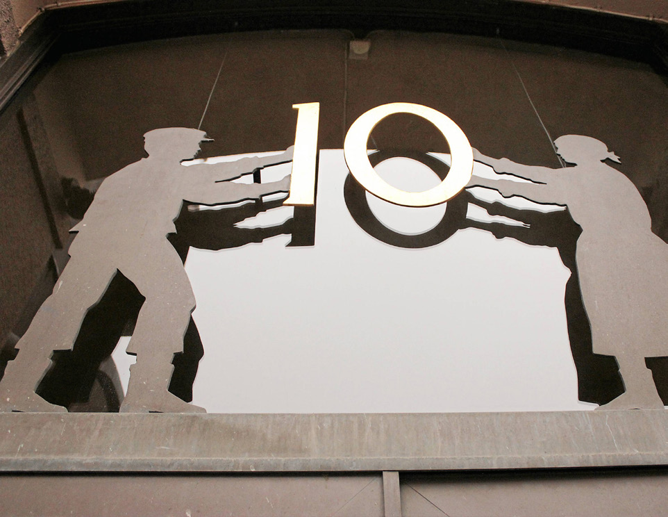 Siffran 10 ovanför A-kassans lokaler på Banhusgatan. Siffran hålls uppe av två silhuett-skulpturer i metall.