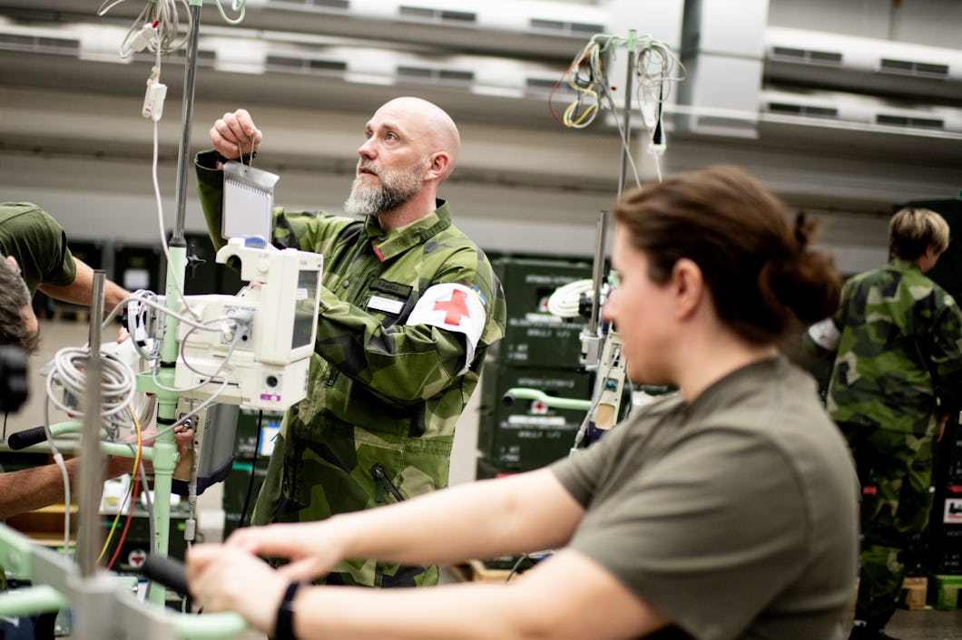 En person i kamouflakeuniform hänger upp en droppåse på en ställning.