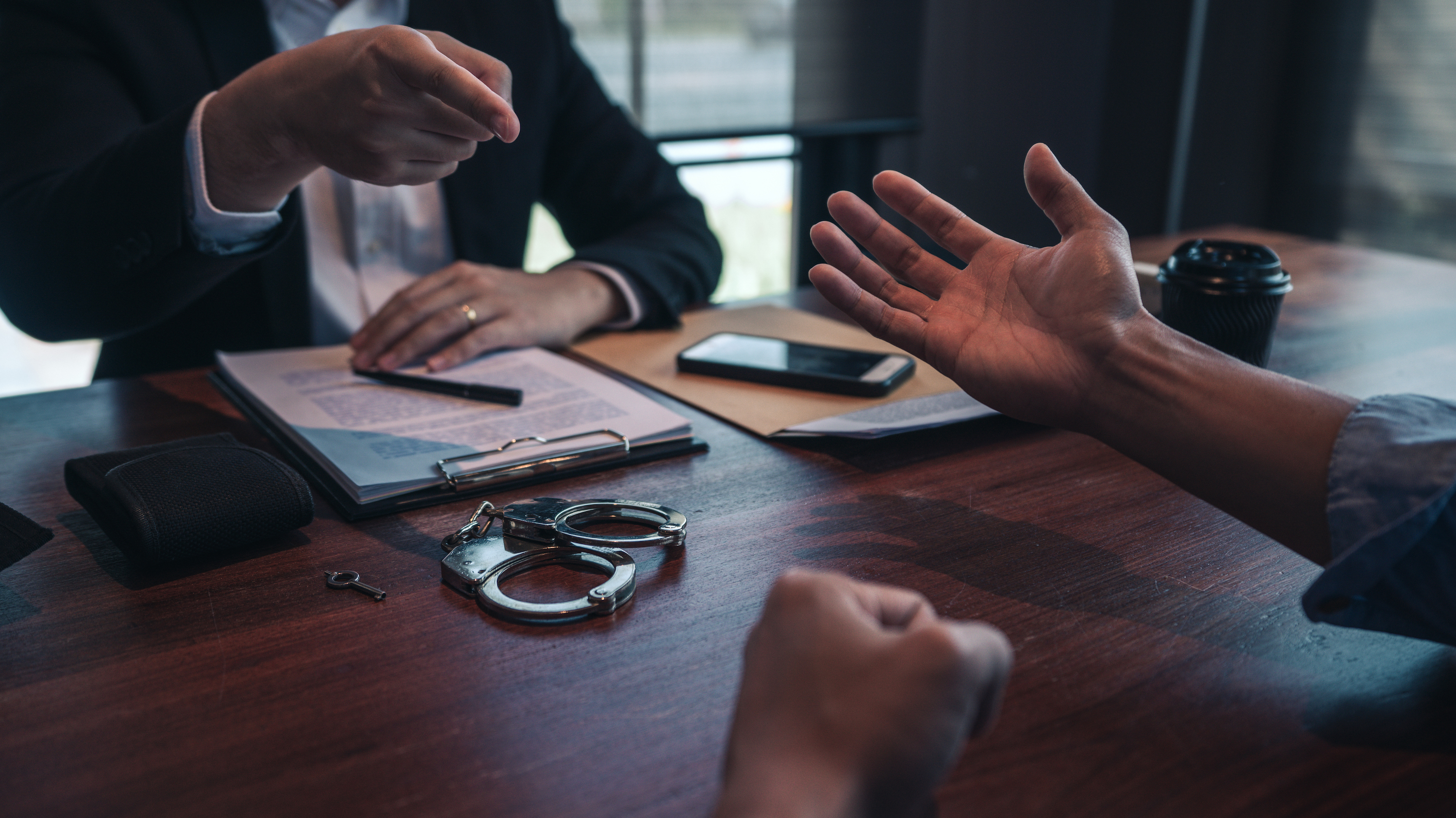 En person pekar anklagande på en annan person över ett skrivbord med handklovar på.