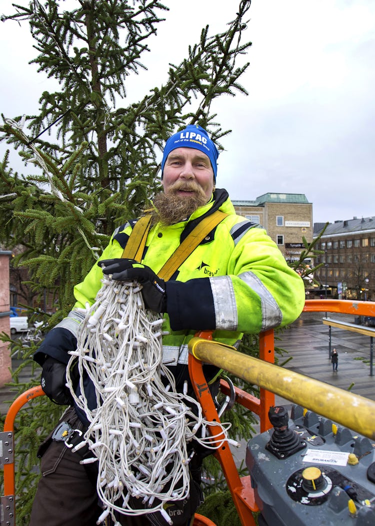 Patrik Jansson uppe i skyliften vid granens topp, hållandes en lång ljusslinga