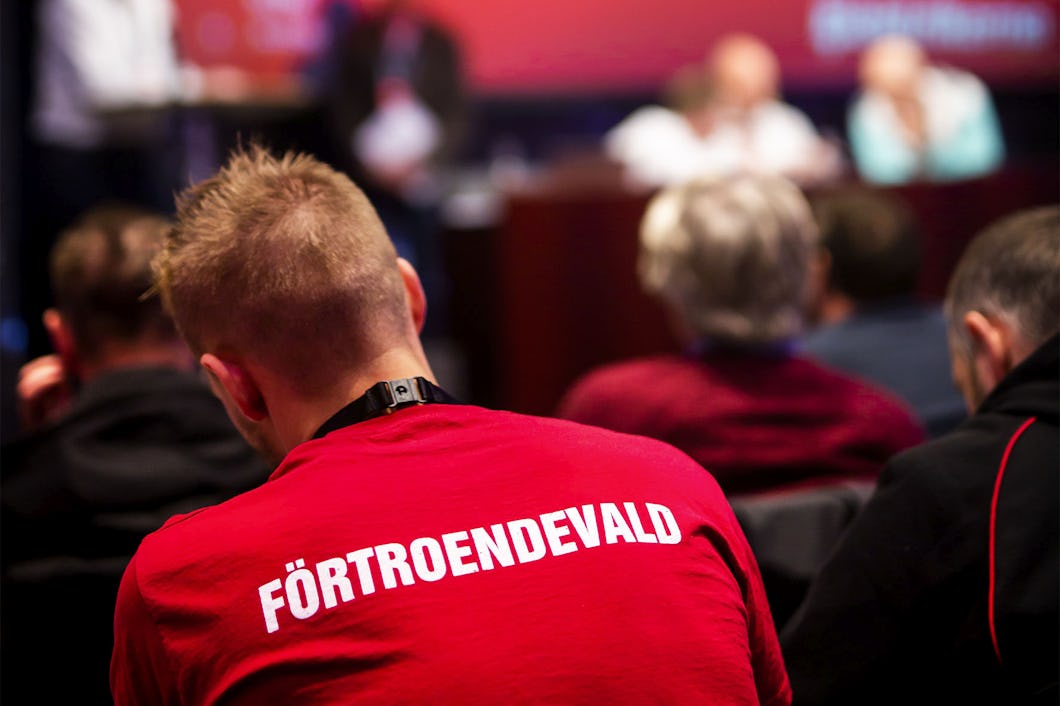 Ryggtavlan på en person på ett möte. Personens tröja är röd och har ordet "Förtroendevald" tryckt i vita bokstäver.