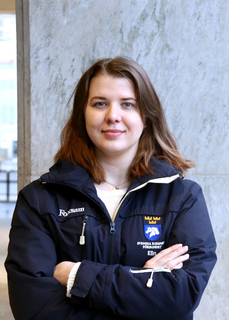 Elin Larsson står med armarna i kors utomhus i stadsmiljö