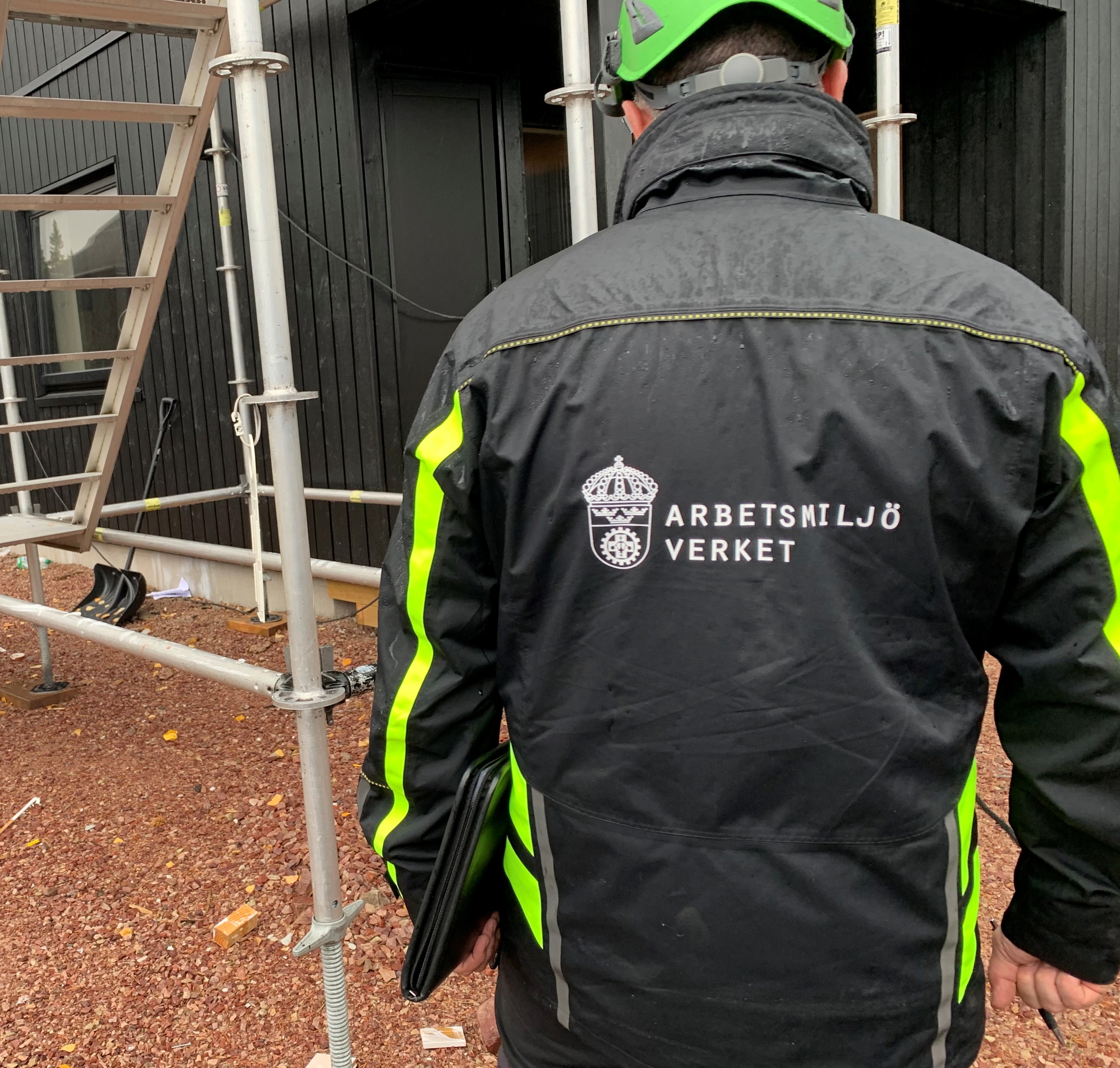 En person i Arbetsmiljöverkets jacka och hjälm på en byggarbetsplats