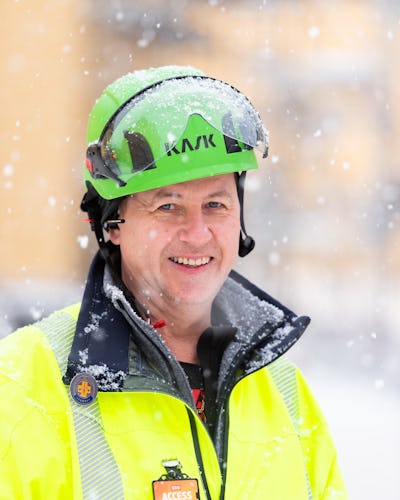 Mikael Olsson utomhus i snön, iklädd grön hjälm och gul reflexjacka.