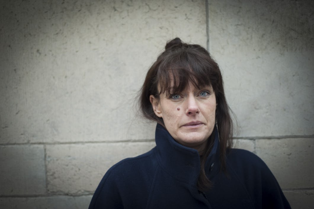 Maria Nyberg i närbild mot vit vägg. Bär mörkblå kappa.