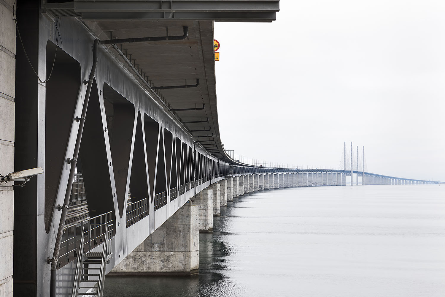 Öresundsbron snett underifrån på högra sidan, med vatten på vänstra sidan.