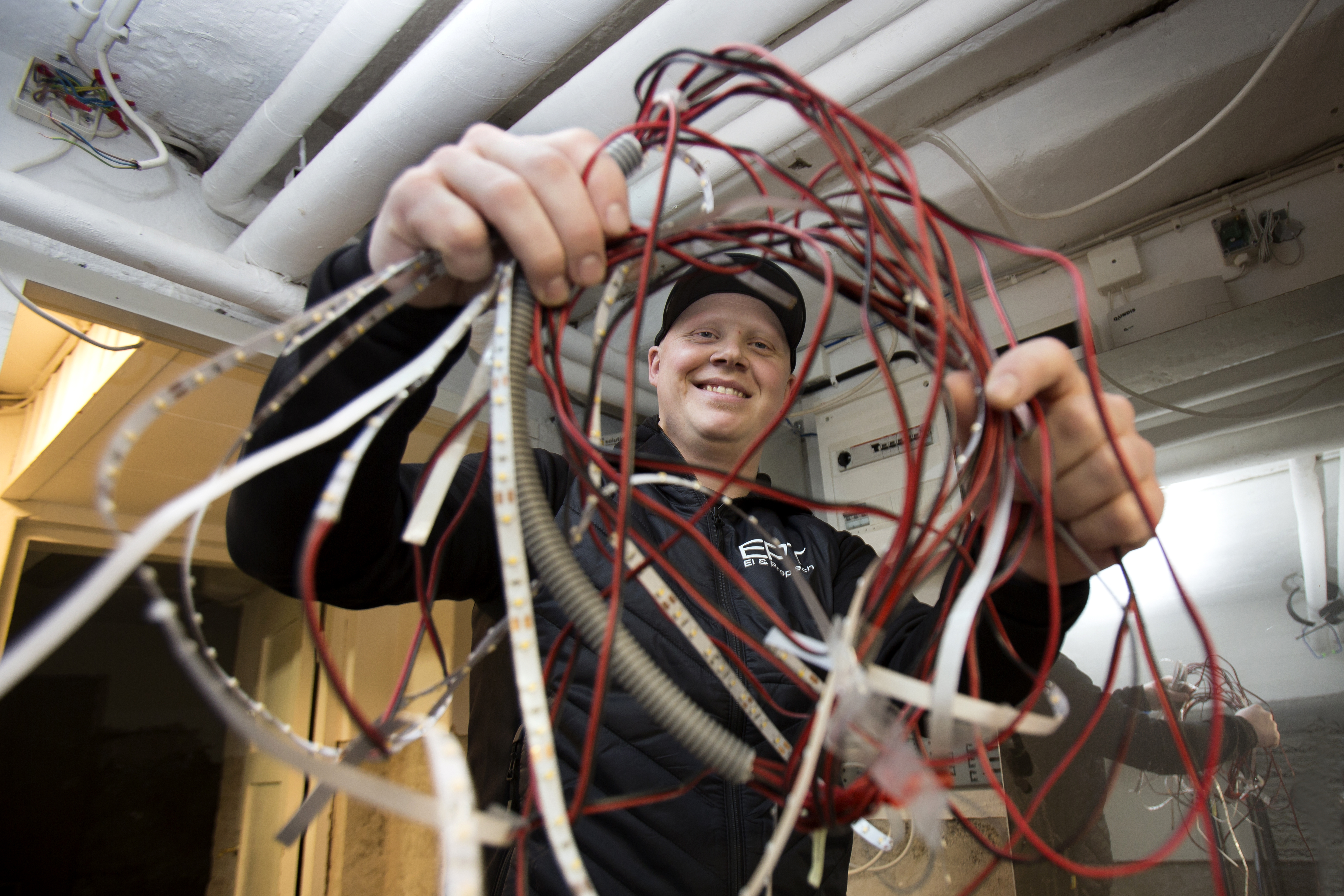 En glad ung man som håller i en bunt sladdar, han tittar igenom dom och in i kameran.