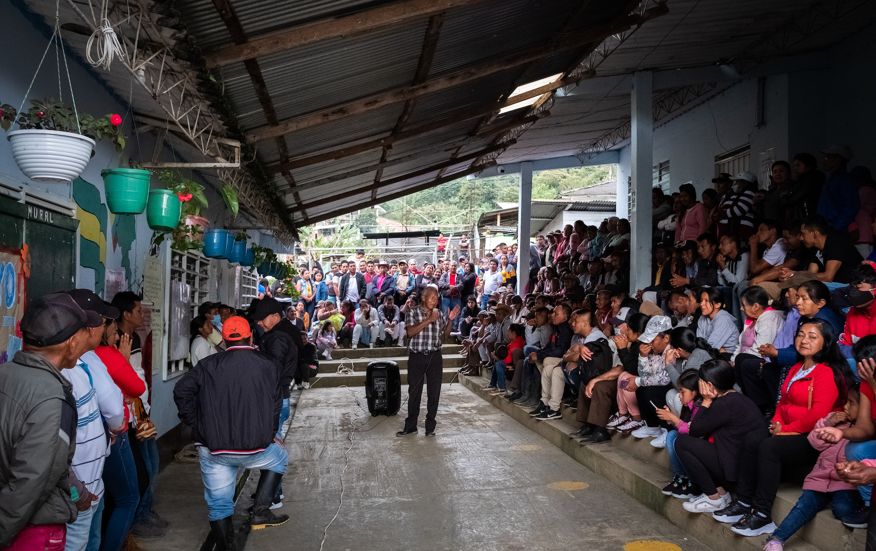 En äldre man i rutig skjorta talar framför åhörare som sitter på betongtrappor runtom honom.