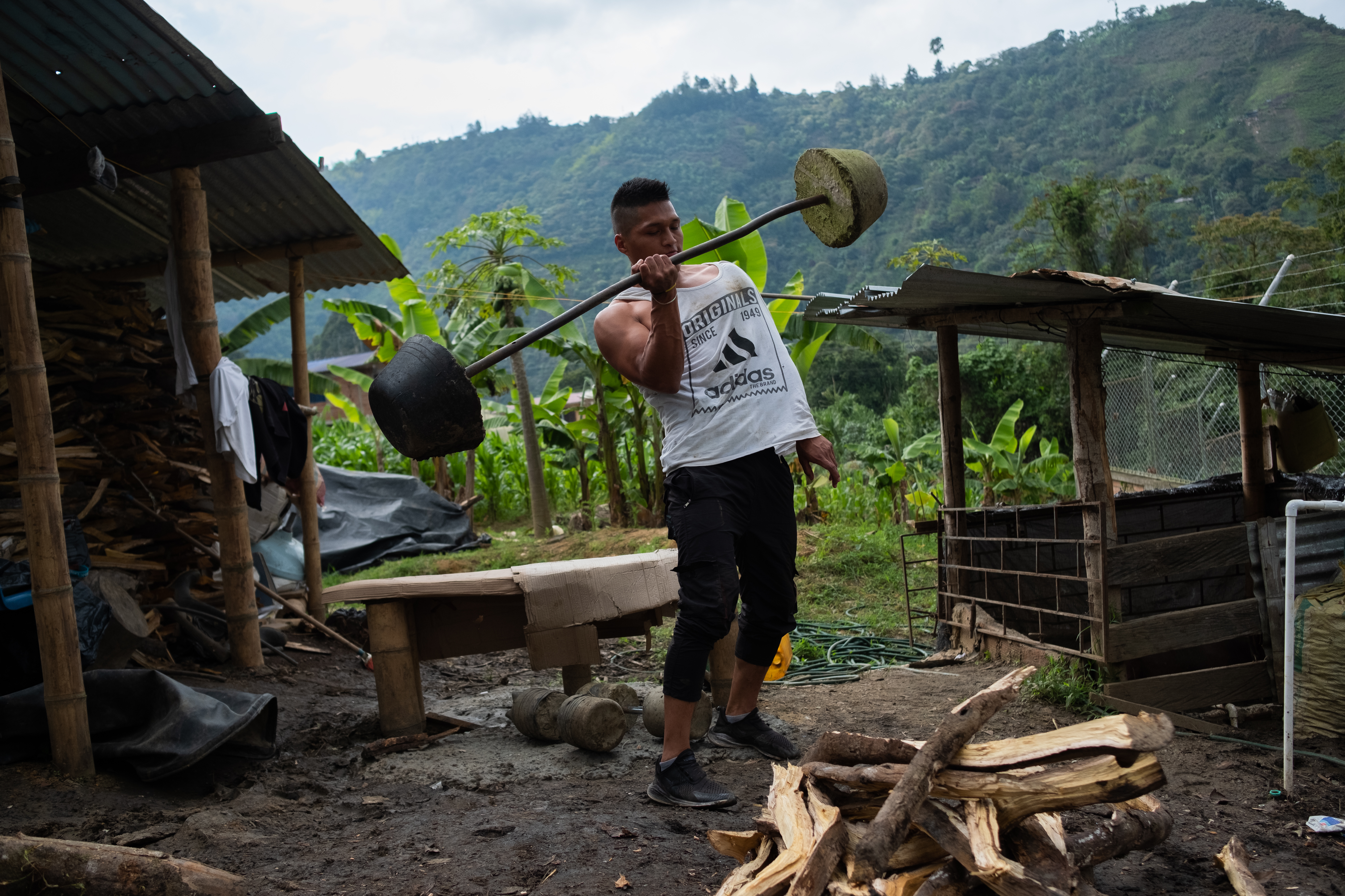 En ung man tränar på gården till ursprungsfolket Nasas huvudkontor. Han är muskulös, klädd i vitt linne och lyfter en hemmabyggd skivstång med ena handen.