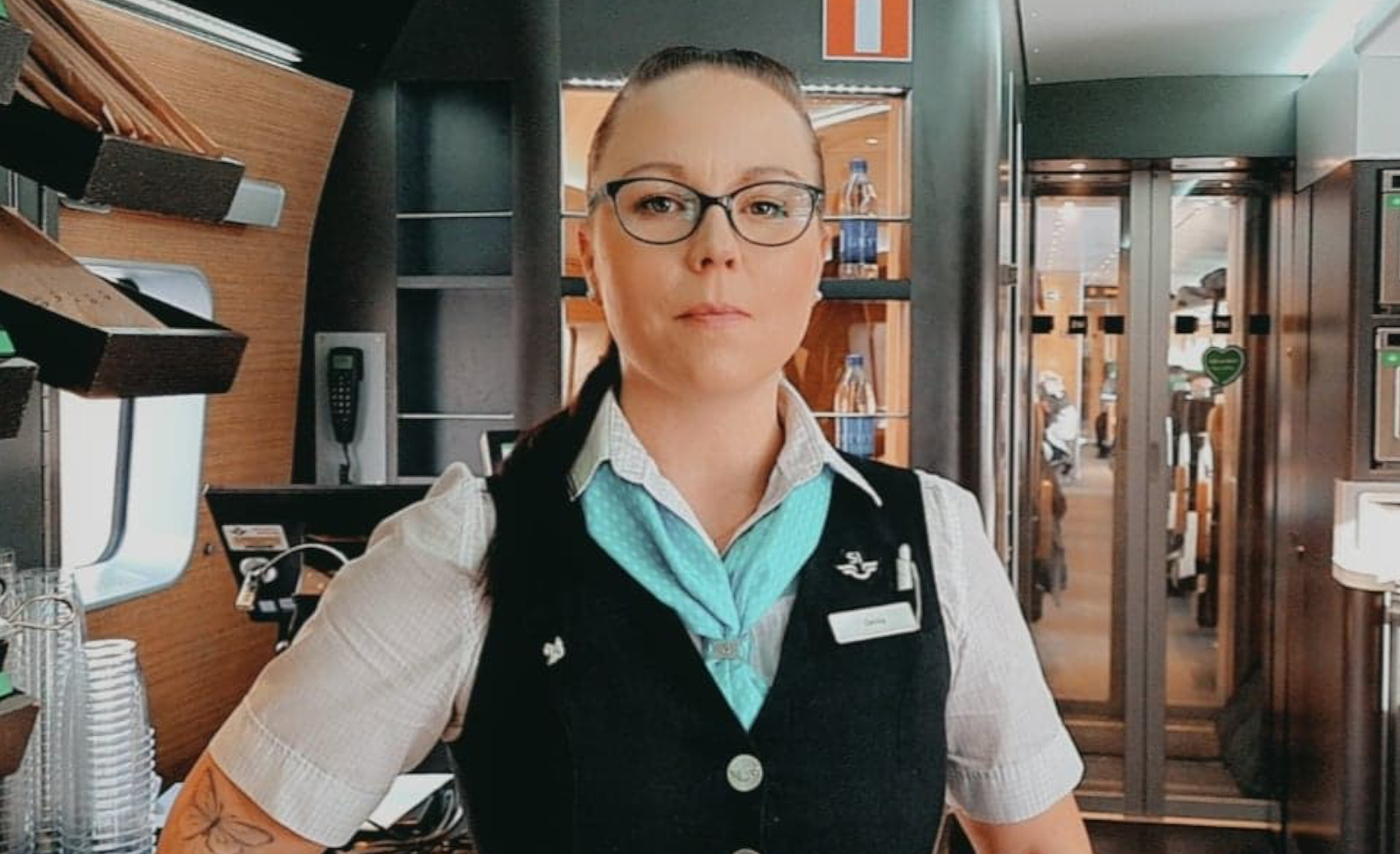 Halv kroppsbild på tågvärden Cecilia Gibson, hon är iförd SJs uniform och står i en tågvarn.