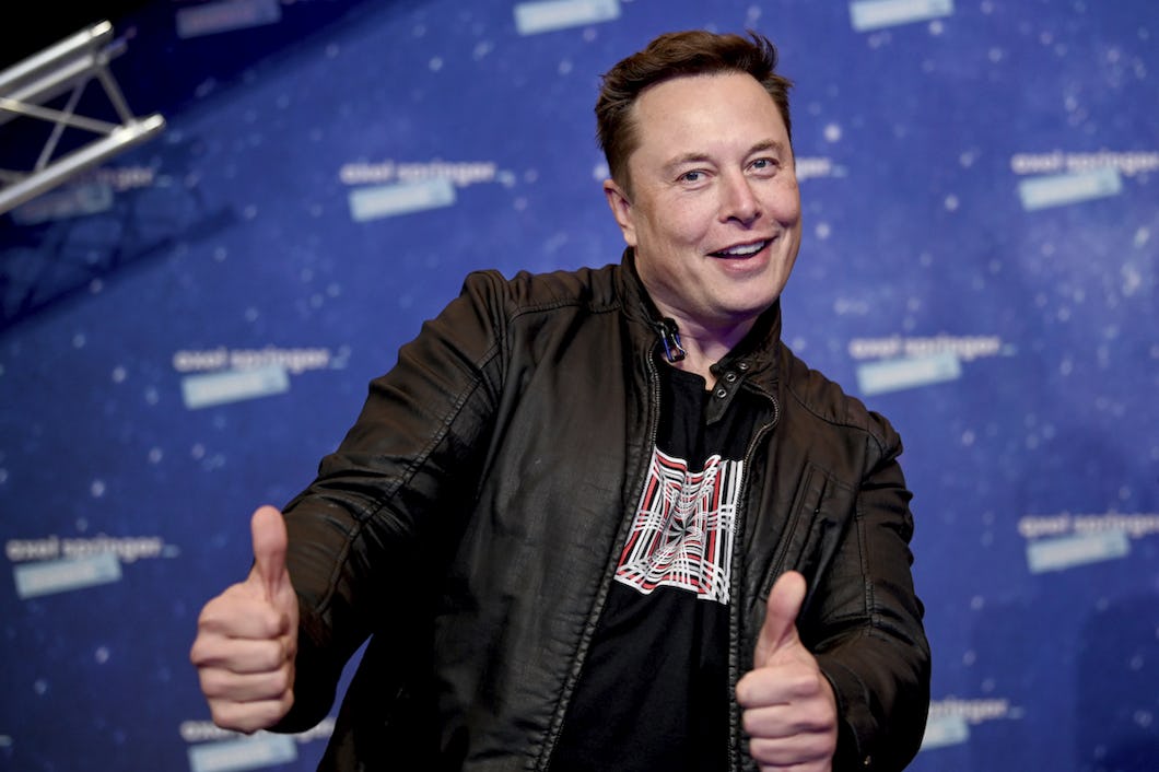 Teslachefen Elon Musk ler snett och gör tummen upp med bägge händerna, klädd i svart läderjacka.