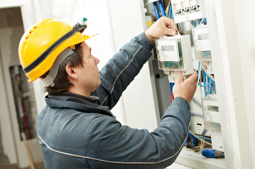 En man i gul skyddshjälm installerar en elmätare.