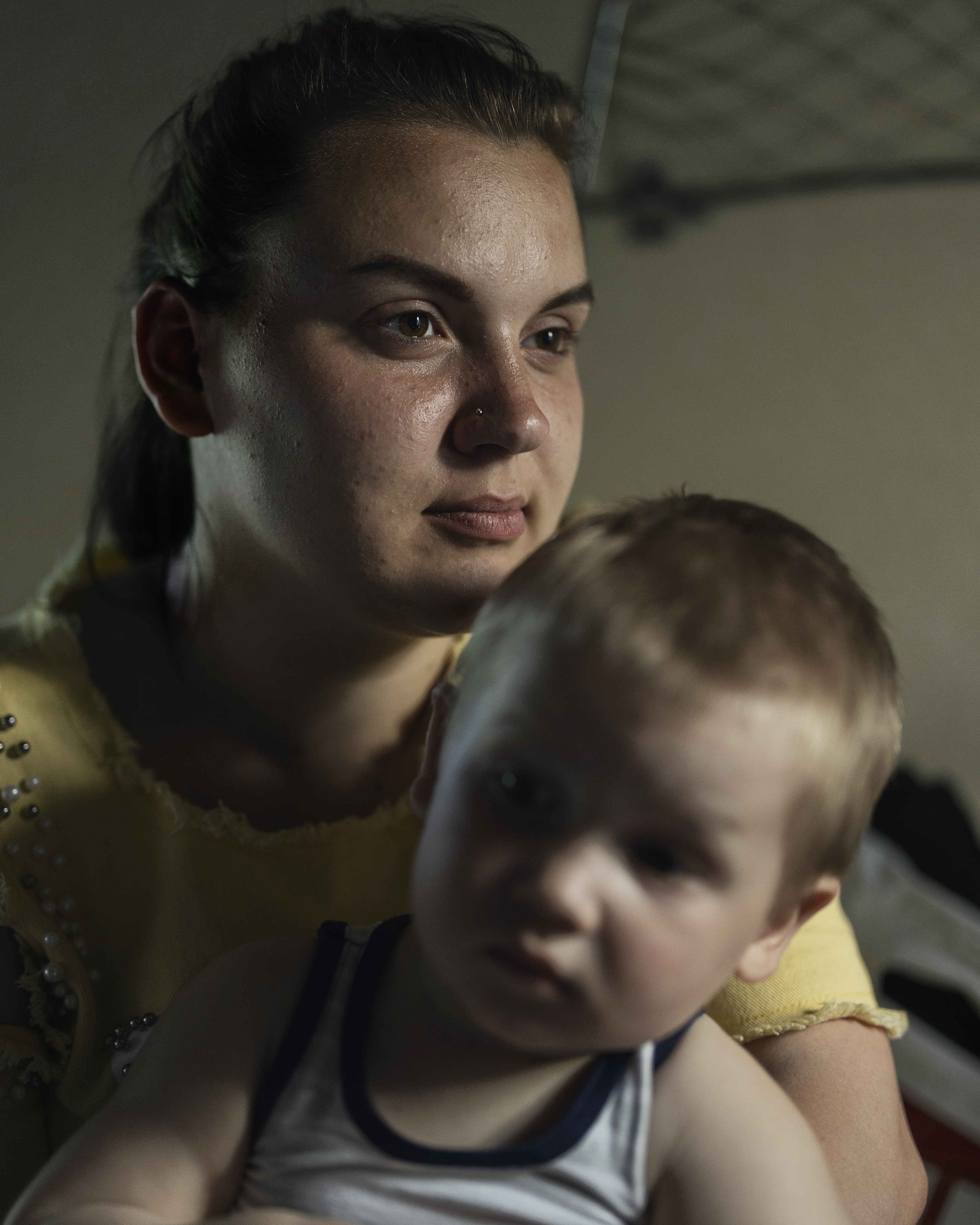 En ung mörkhårig kvinna i gul klänning sitter med ett litet barn i famnen.