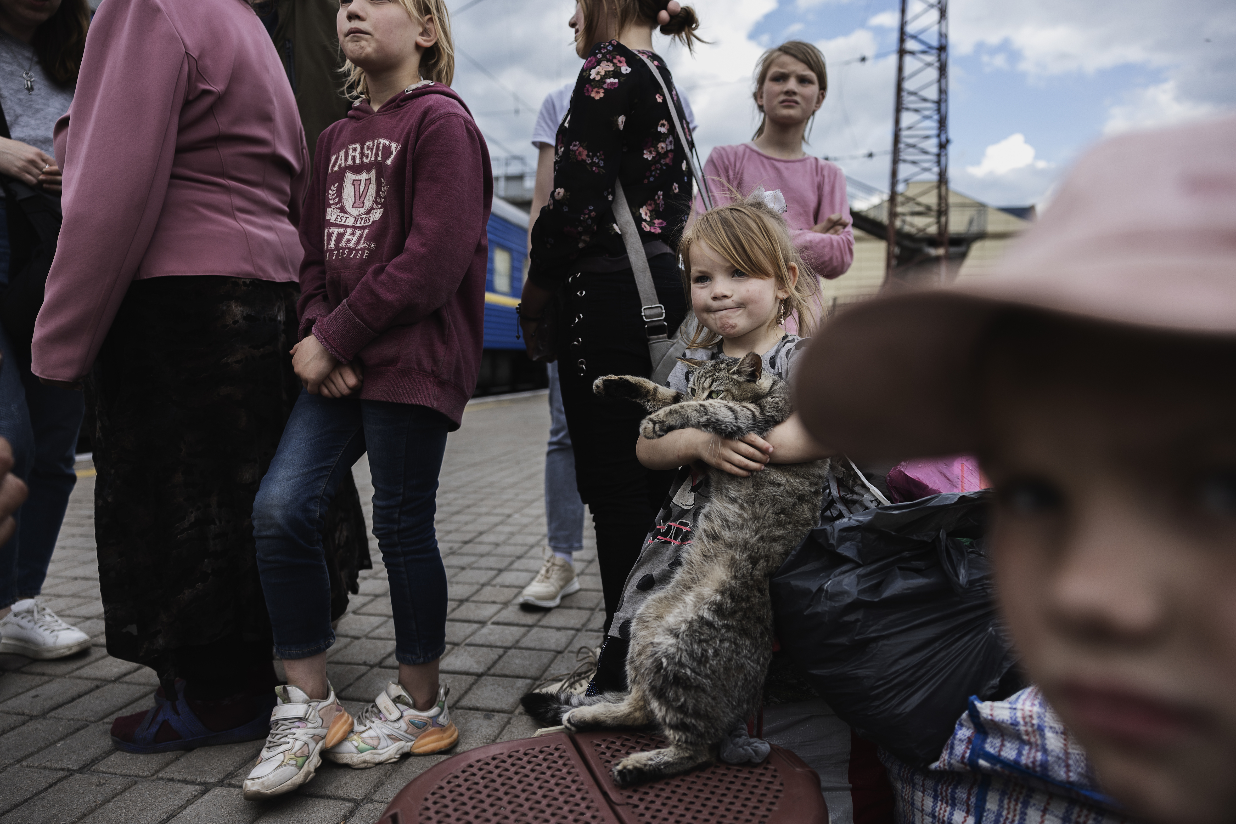 En liten flicka lyfter en katt i famnen på en tågperrong. Runt om henne står äldre syskon.