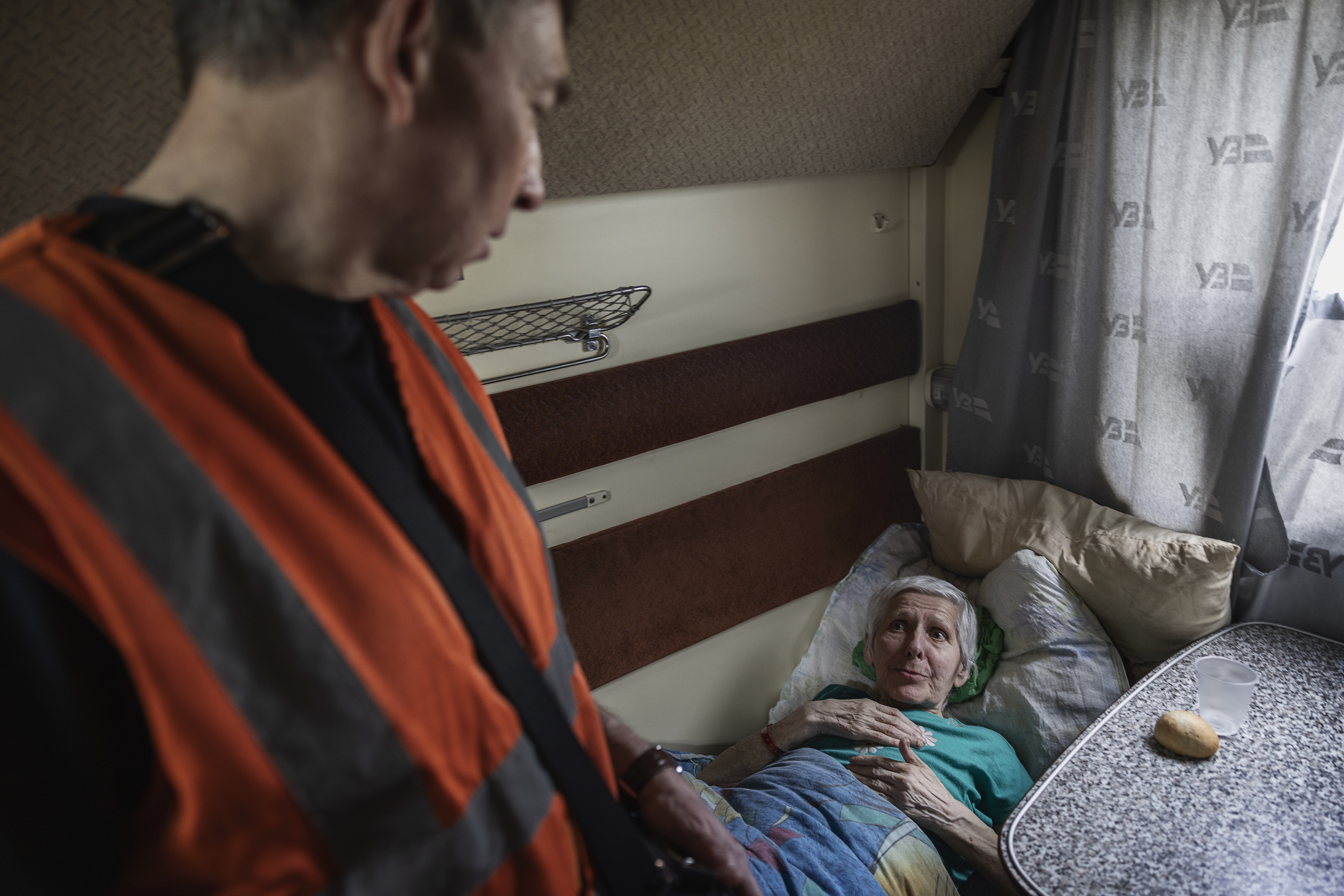 En läkare i orange väst pratar med en äldre kvinna som ligger på en slaf i en tågkupé.