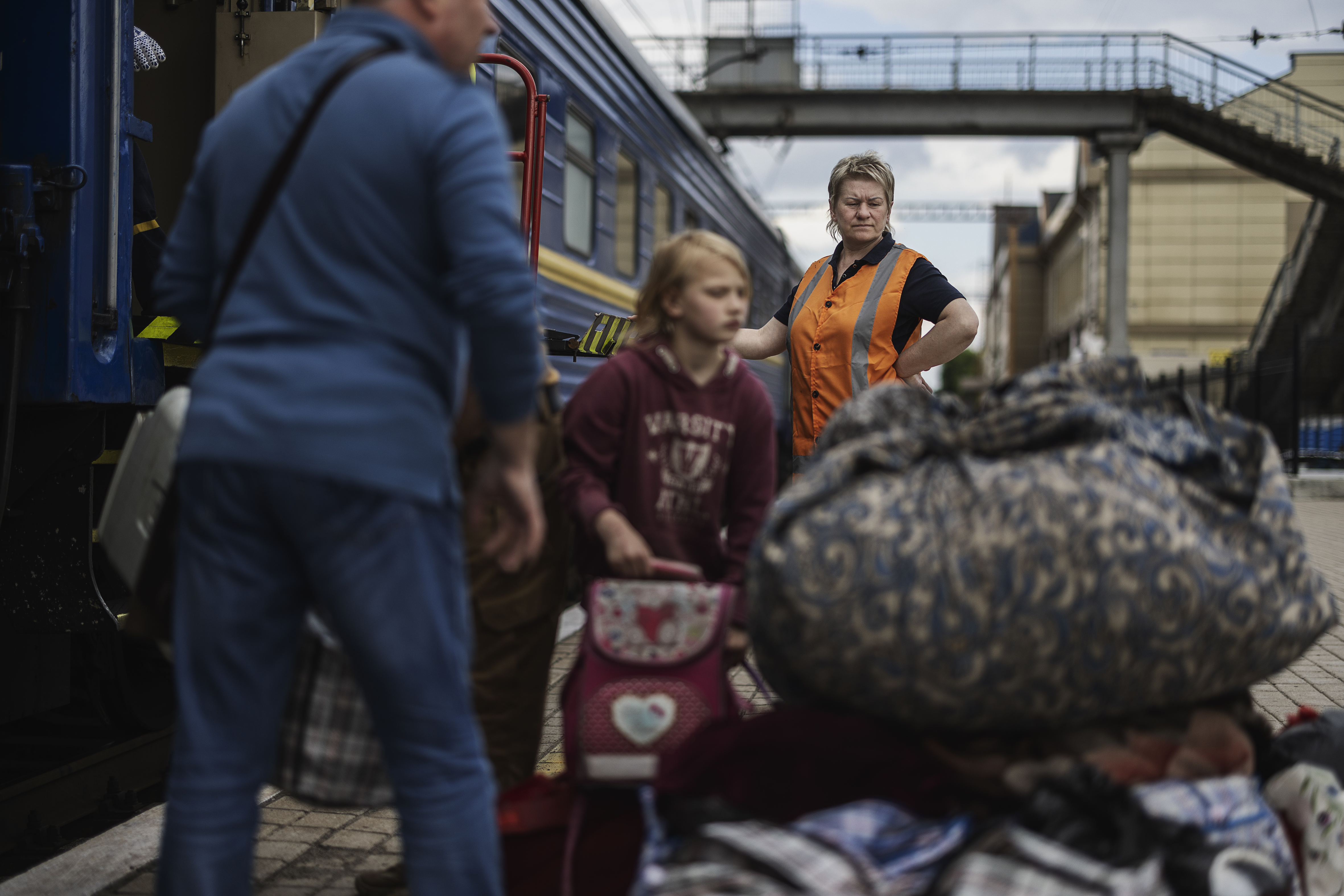 En blond medelålders kvinna från järnvägsbolaget ser på medan flyktingar lastar ombord sina väskor på tåget.