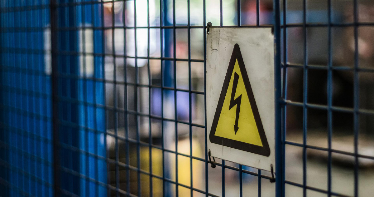 En gul varningsskylt med svart blixt, på ett gallerstängsel.