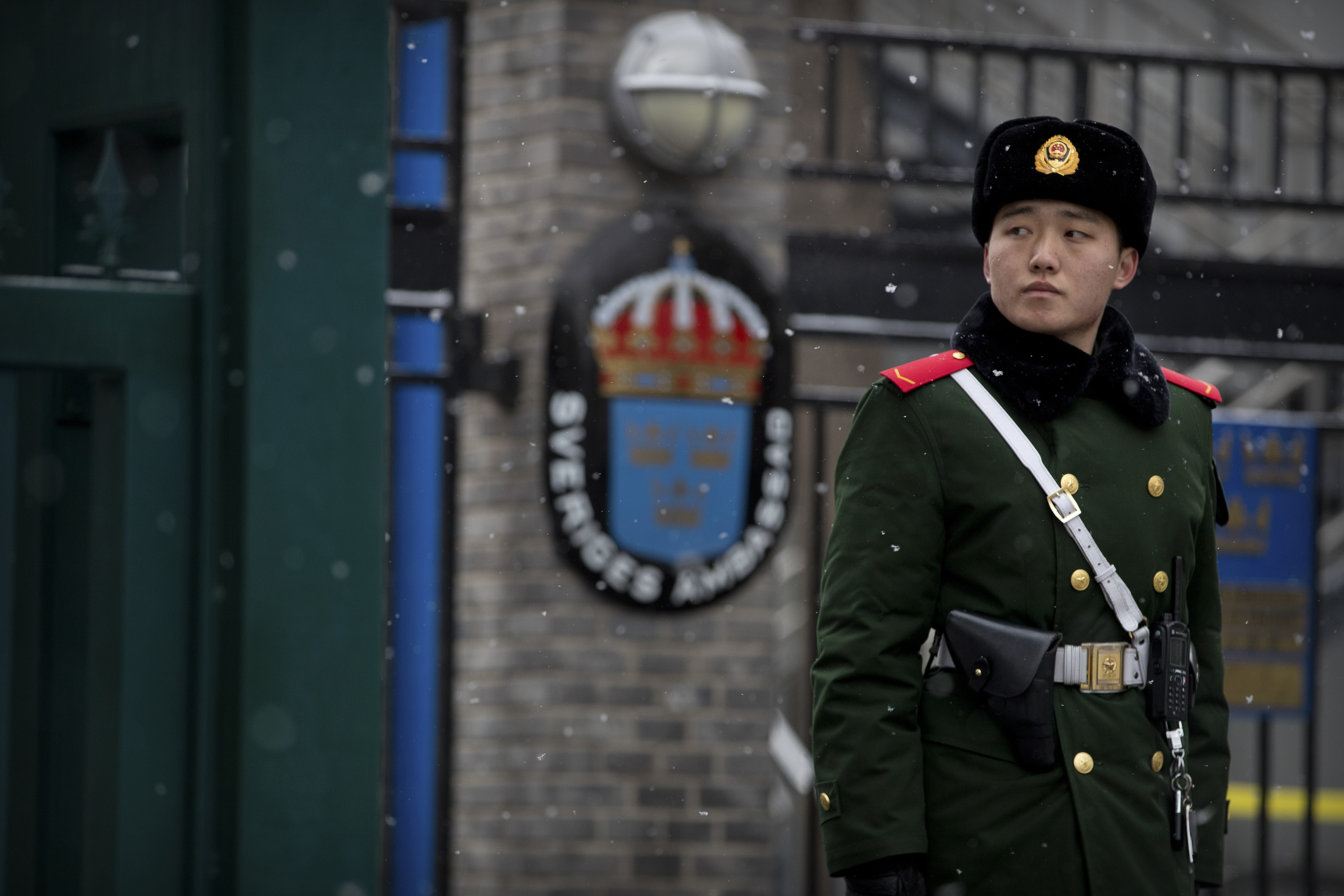 En militär står på vakt, svenska ambassadens logga syns suddigt i bakgrunden.