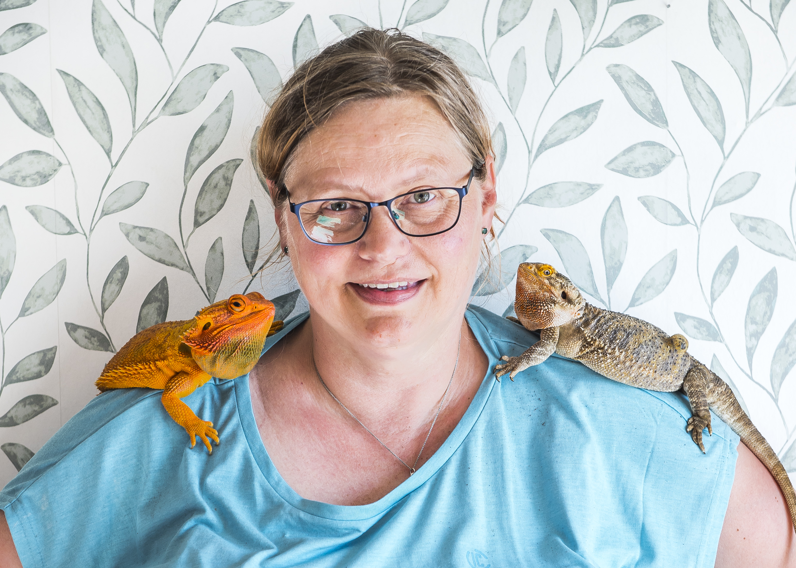 Tågvärden Britt-Inger Rydland med två färgglada ödlor på varsin axel.