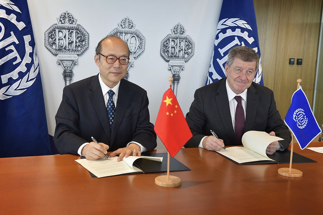 Kinas FN-ambassadör Chen Xu och ILO:s chef Guy Ryder undertecknar varsitt papper vid ett skrivbord.