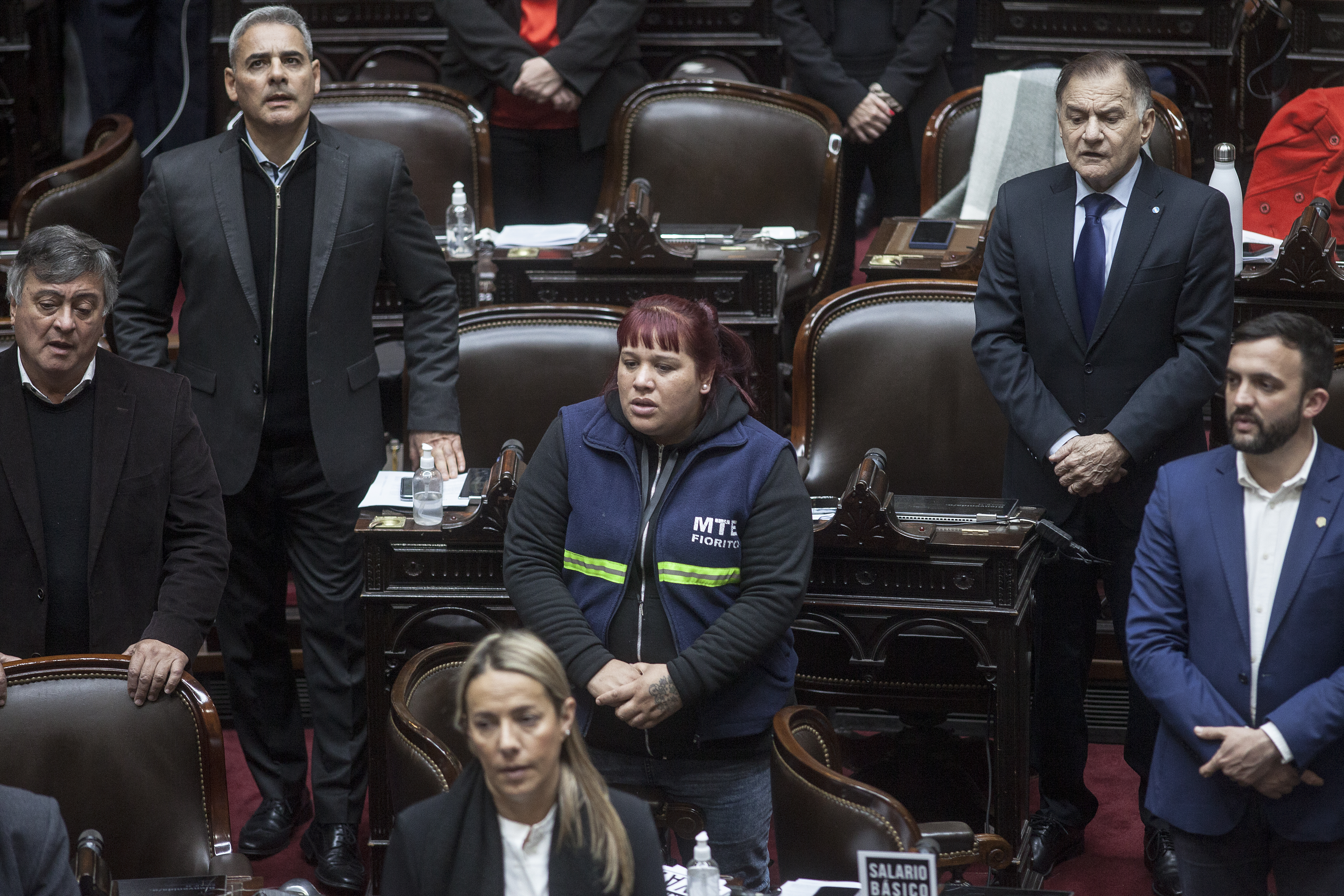 Natalia Zaracho sjunger nationalsången i Argentinas parlament. Hon bär arbetsuniform och är omgiven av parlamentariker i kostym.