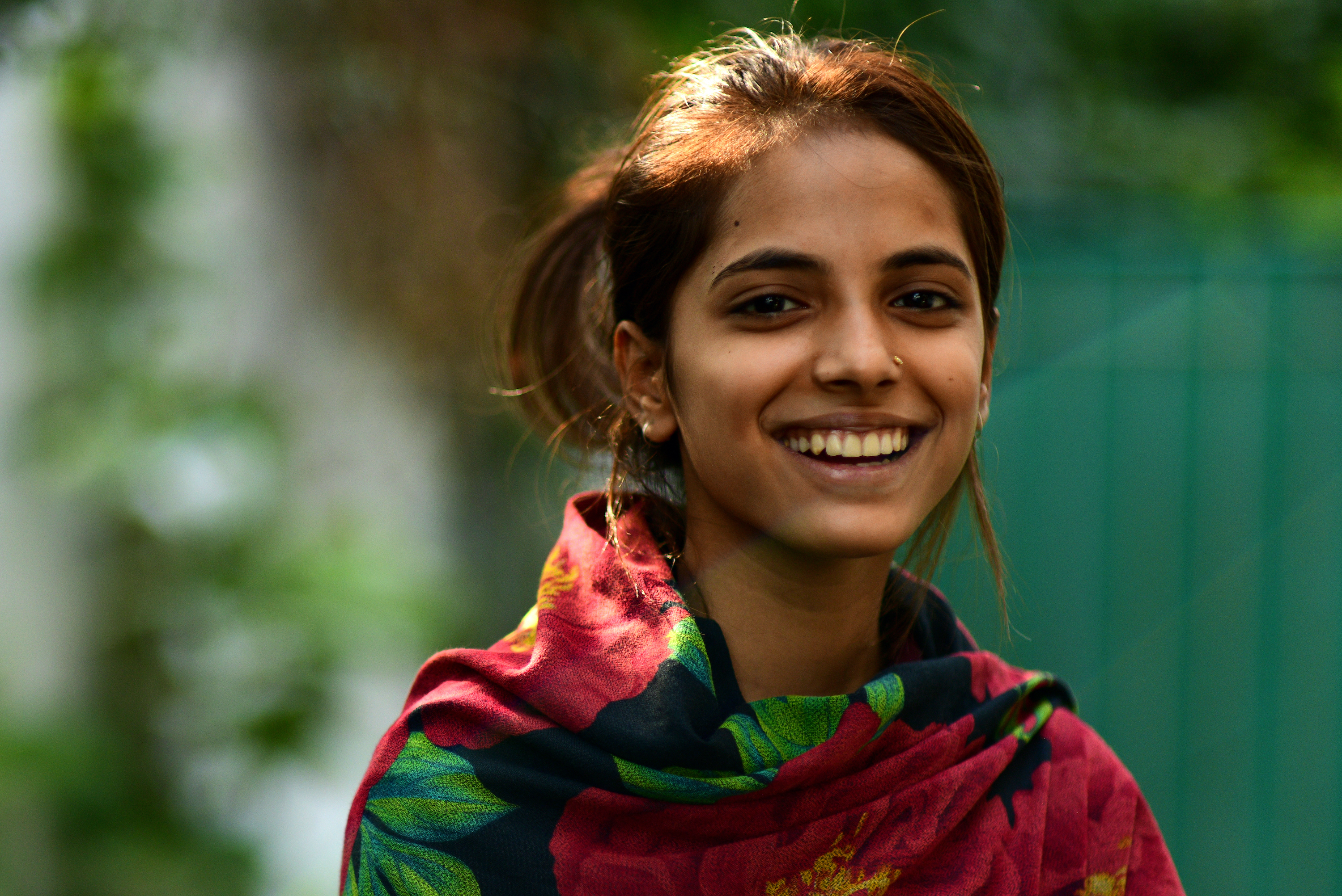 En ung pakistansk kvinna med färgglad sjal runt axlarna ler mot kameran.