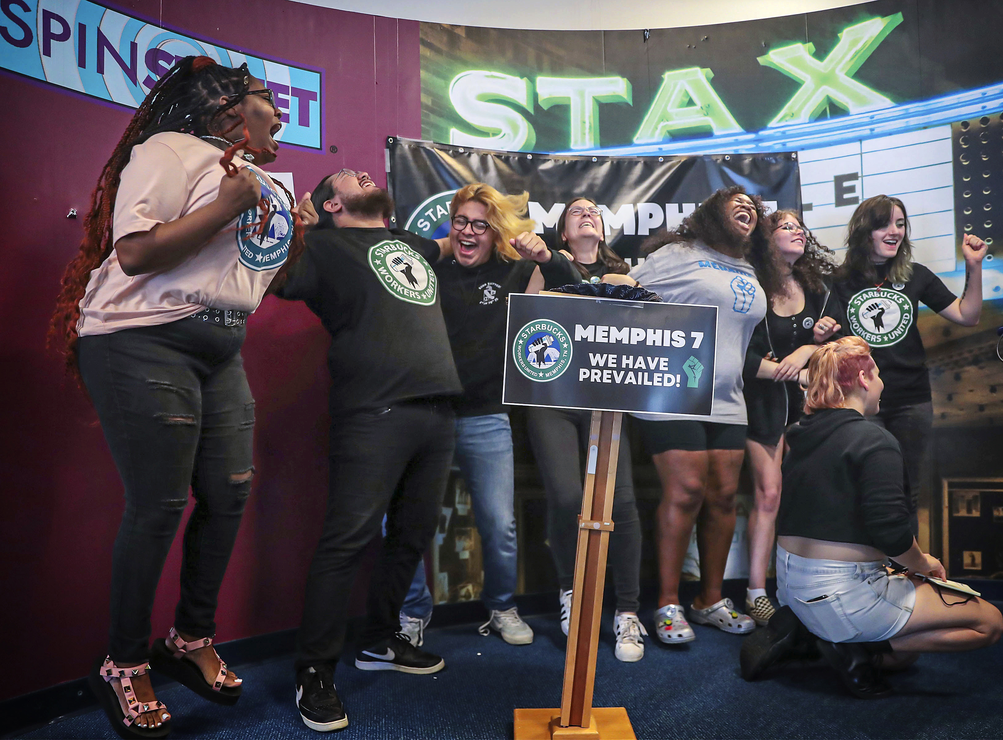 Sju män och kvinnor håller armarna om varandra och jublar. Flera har t-tröjor med sin fackförenings logotyp.