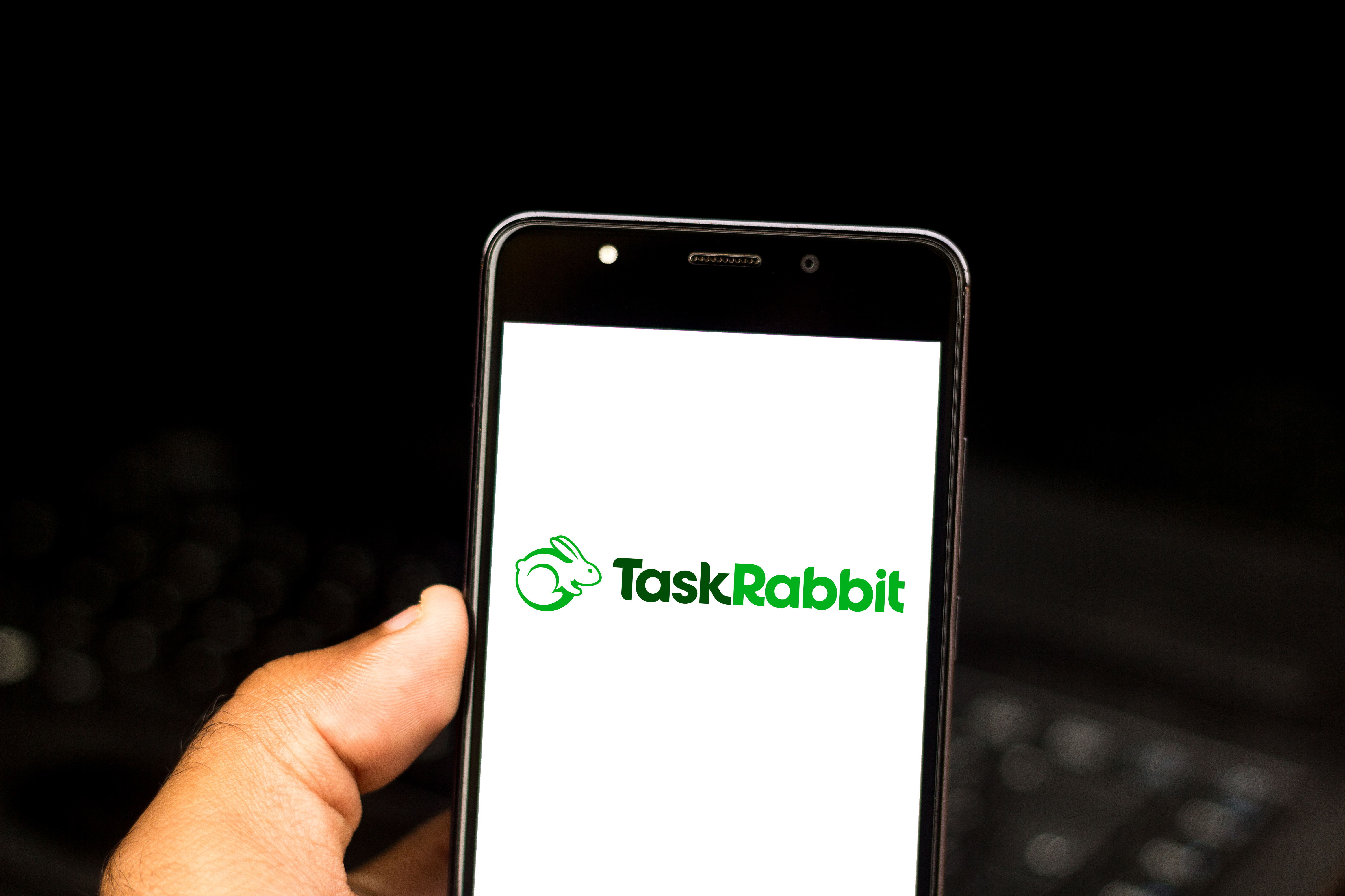 En hand håller upp en mobiltelefon, skärmen visar Taskrabbits logga.
