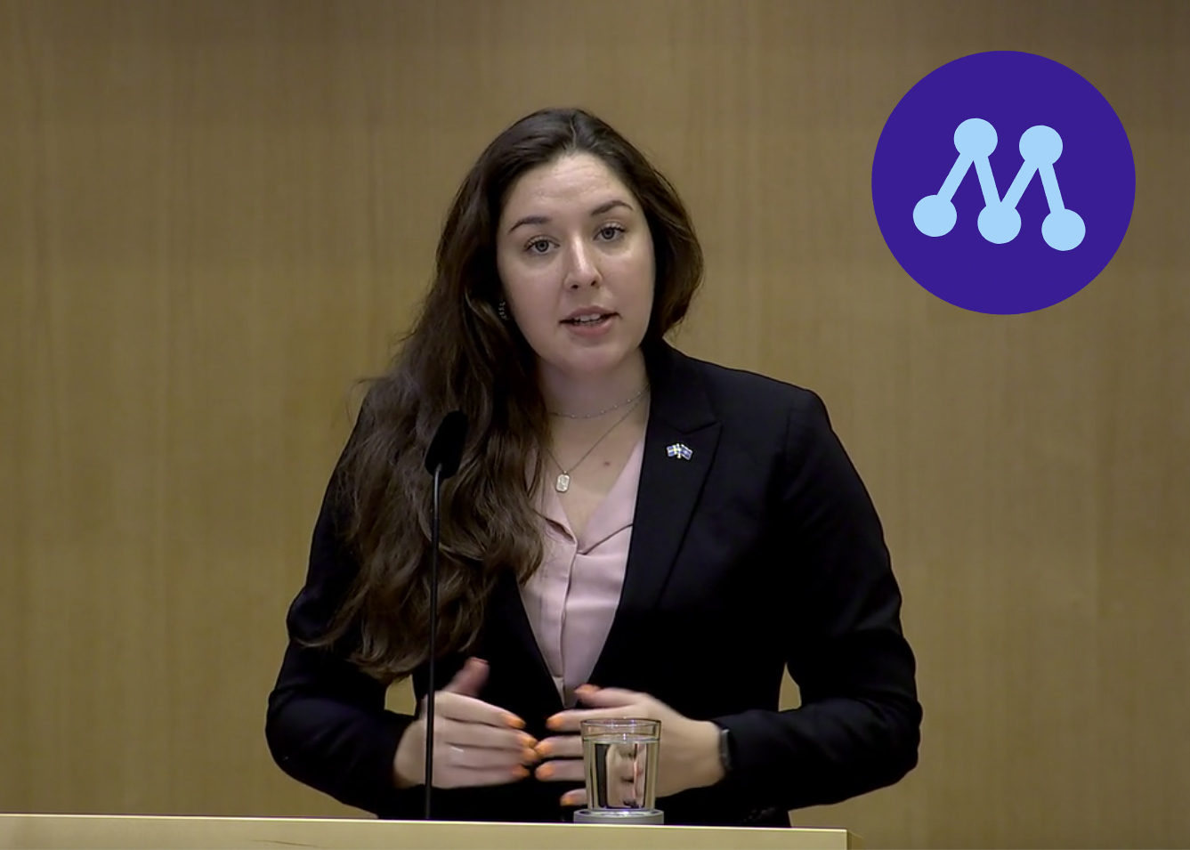 Helena Storckenfeldt i riksdagens talarstol, Moderaternas logotyp inlagd i bilden