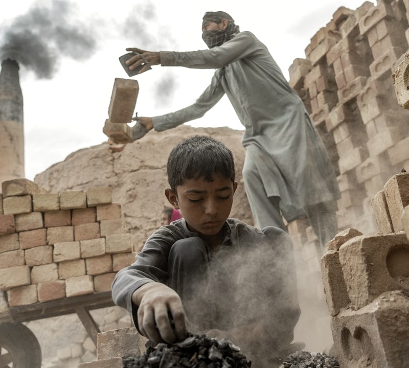 En barnarbetare jobbar i tegelfabriken i Afghanistan, i bakgrunden syns en vuxen arbetare.