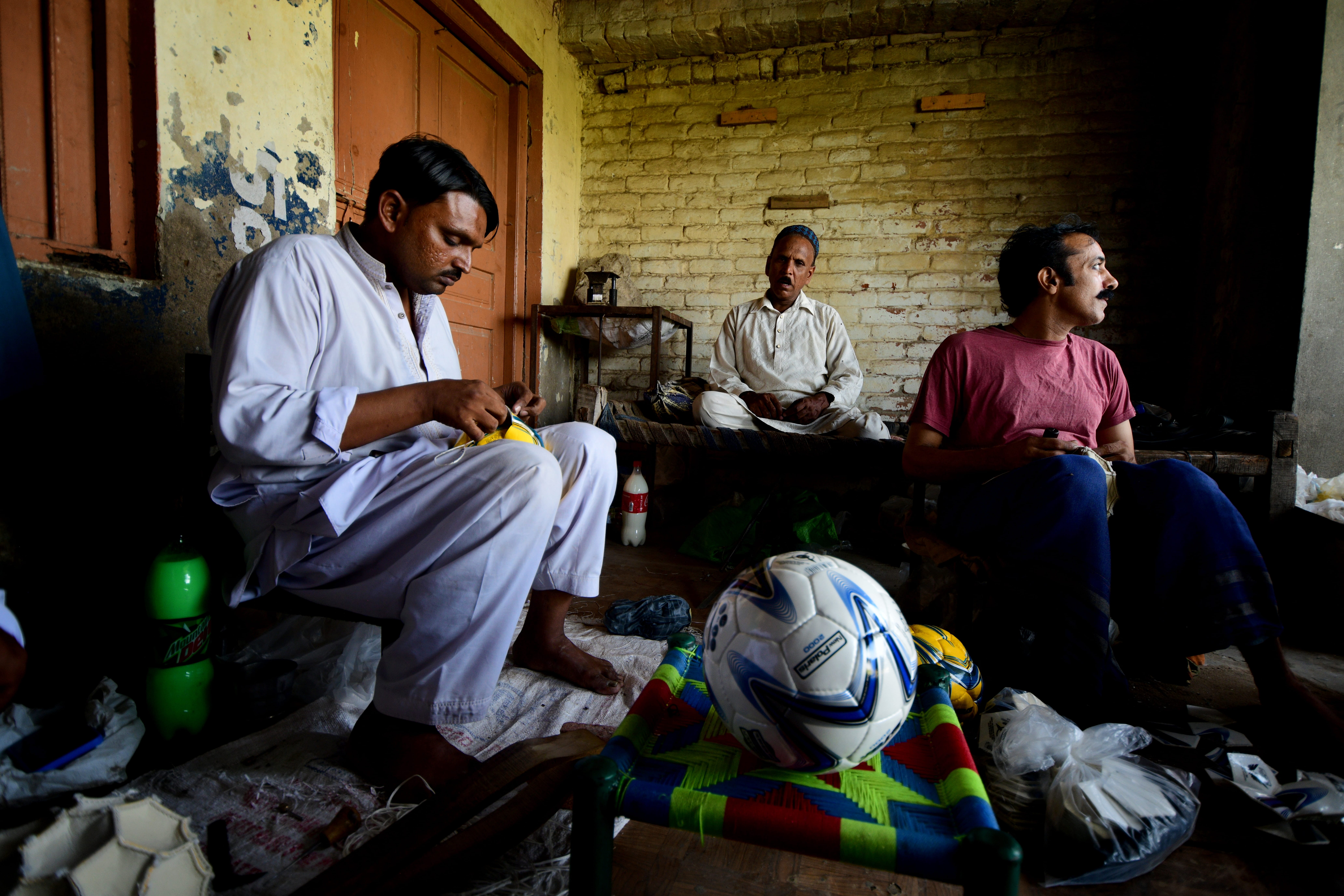 Några män sitter och syr fotbollar.