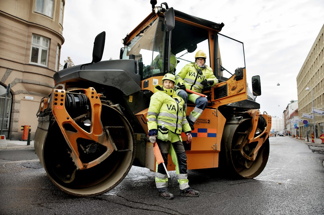 Signalvakterna Jeanette Lundberg och Annica Björk i gula varselkläder framför en stor orange asfaltsvält.