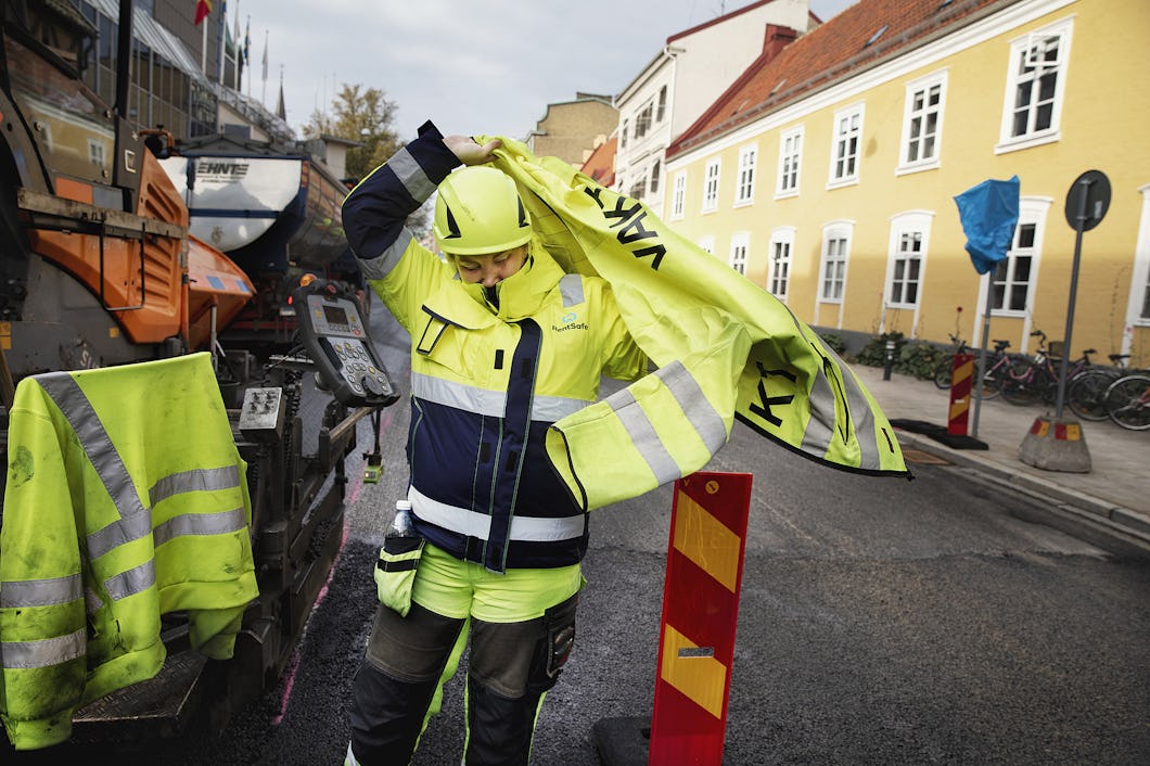Vägarbetare i gula varselkläder, som håller på att ta på sig en gul väst ovanpå jackan.