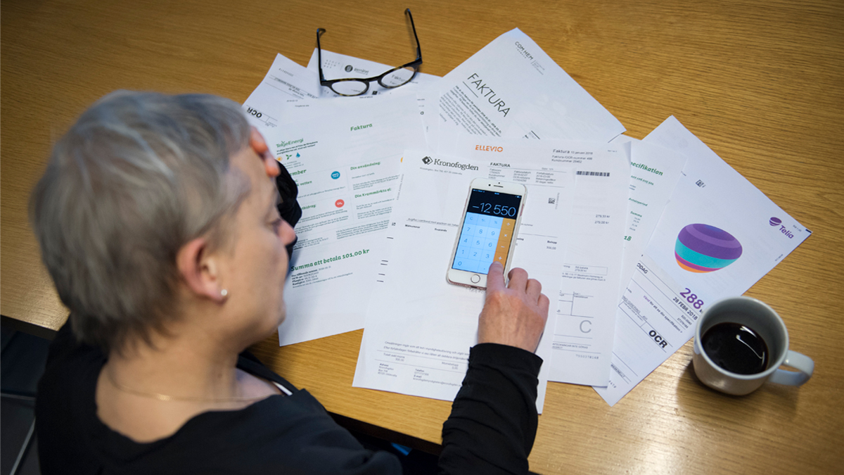 Kvinna sitter med en hög räkningar och en miniräknare framför sig.