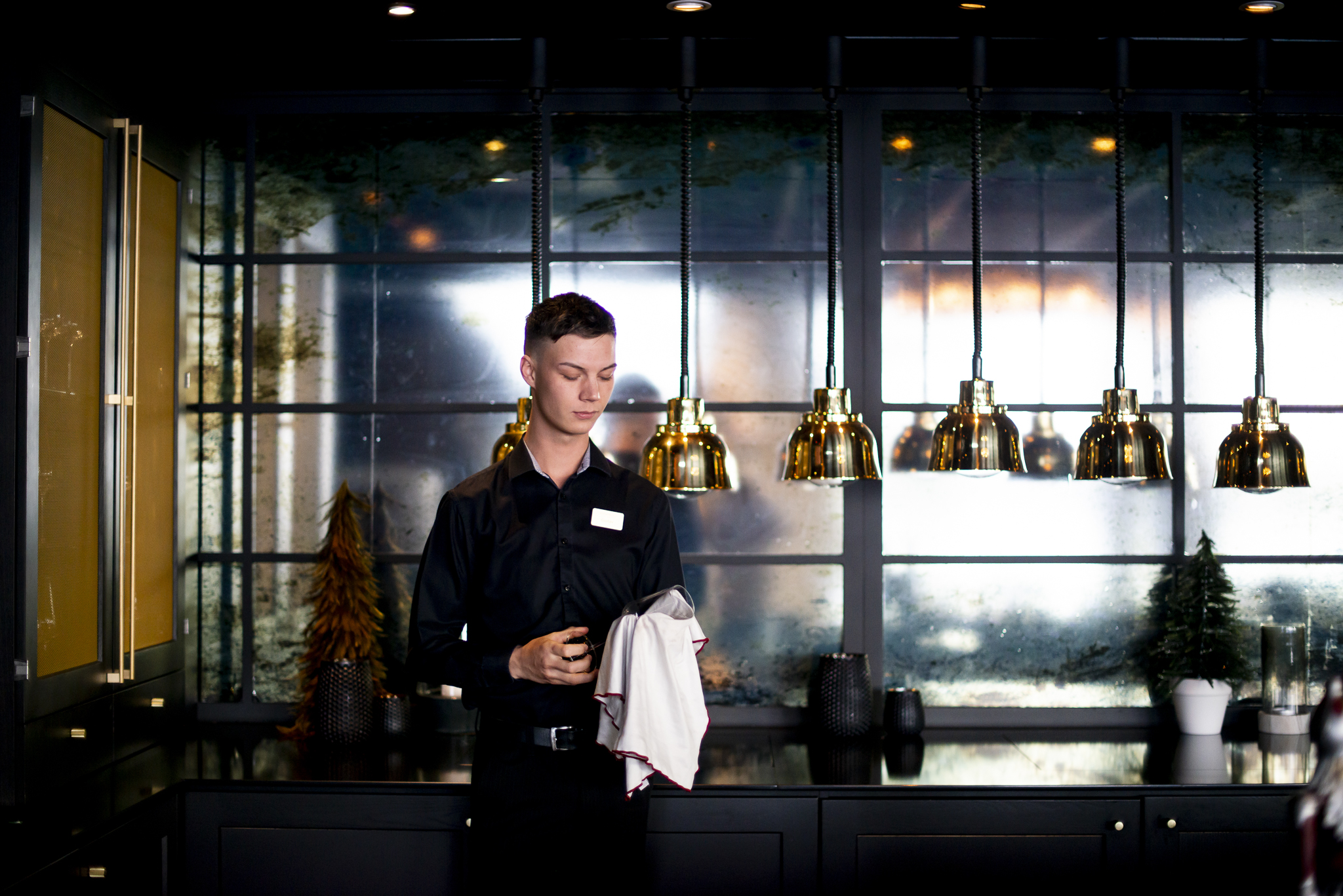 Gustav står i en restaurang där han jobbar och torkar ett glas.