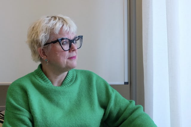 Suzann sitter i en fåtölj i grön treja och tittar ut genom fönstret i sitt mottagningsrum.