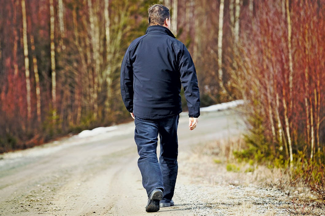 Vi ser ryggen på en man som promenerar på en skogsväg.