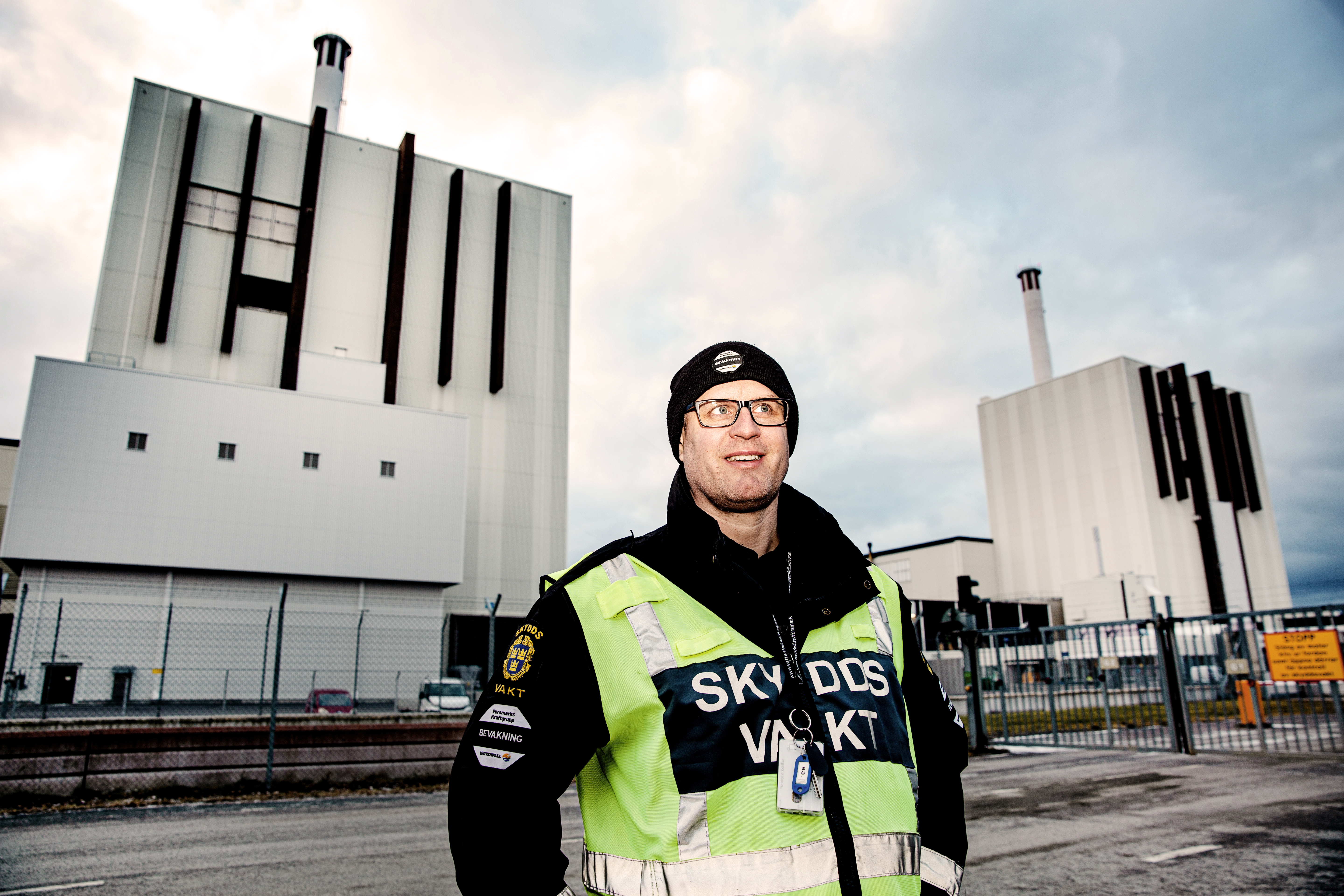 Skyddsvakten Henrik i gul varselväst framför Forsmarks reaktor 1. I bakgrunden syns även grinden in till reaktorområdet.